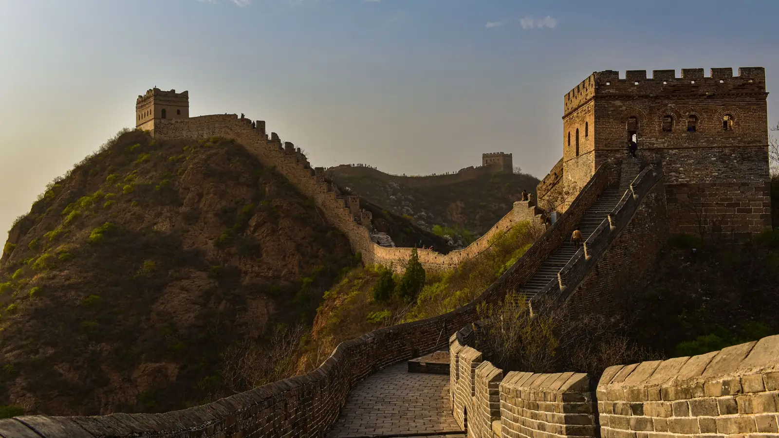 The restored Great Wall with its watchtowers snaking along a forested mountain ridge in warm golden light